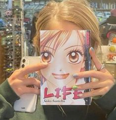 a woman holding up a book in front of her face with an anime character drawn on it