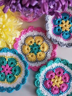 four crocheted coasters with flowers in the middle on a white table top