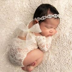 a newborn baby wearing a white lace outfit with a bow on it's head