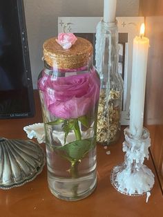 a glass jar with flowers in it sitting on a table next to a candle and seashell