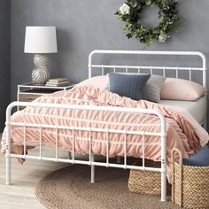 a white bed with pink sheets and pillows in a bedroom next to a wreath on the wall