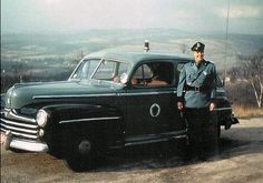 an old photo of a man in uniform standing next to a car on a dirt road