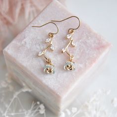 a pair of earrings sitting on top of a pink marble block next to some flowers