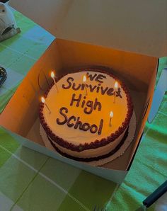 a birthday cake in a box that says we survived high school with lit candles on it