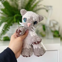 a person holding a small stuffed animal in front of a potted plant with green leaves