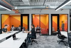 people sitting at desks in an office with orange and yellow dividers on the walls