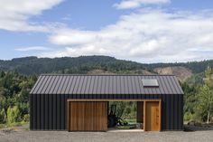 a black building with wooden doors in front of trees and mountains on a cloudy day