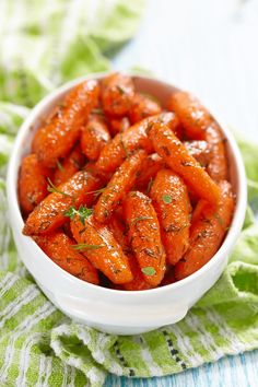 a white bowl filled with cooked carrots on top of a green cloth covered table