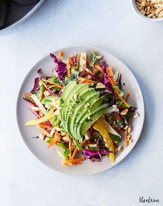 a white plate topped with a salad next to a bowl of nuts and avocado