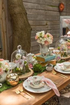 the table is set with tea cups, plates and flowers in glass vases on it