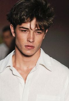 a young man in a white shirt is looking at the camera while he walks down the runway