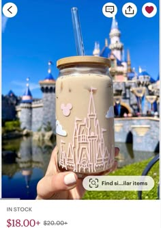 a person holding up a cup with a straw in front of a castle at disneyland