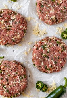 three hamburger patties sitting on top of white paper next to jalapenos