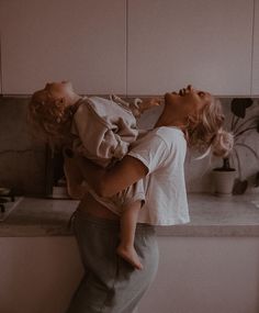 a woman holding a baby in her arms while standing next to a kitchen counter top