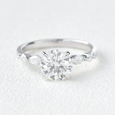 a white gold engagement ring with three stones on the band and a single diamond in the center