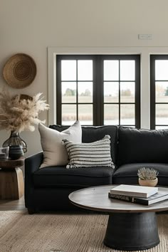 a living room with black couches and pillows on top of the rugs in front of two large windows