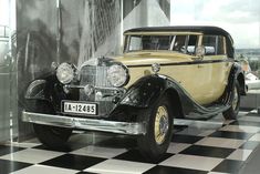 an old model car is on display in a glass walled room with black and white checkered flooring