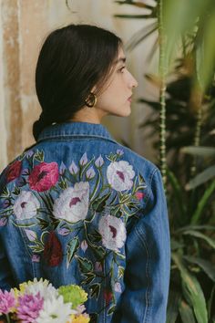 a woman wearing a denim jacket with flowers on it