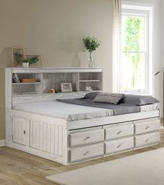 a white bed with drawers underneath it and a window in the backround behind it