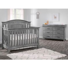 a baby crib and dresser in a room with hardwood floors, gray walls and white rugs