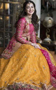 a woman sitting on top of a couch wearing a yellow and pink dress with gold accents