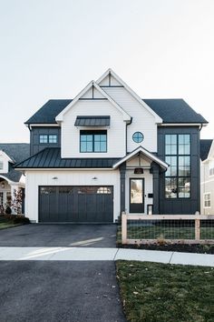 a large white and black house with two garages on each side of the driveway