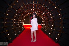 a woman standing in front of a red carpeted tunnel with lights all around her