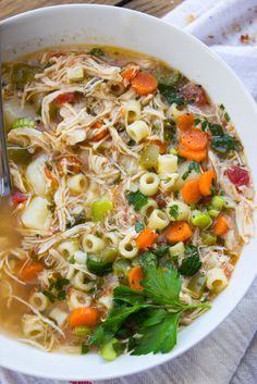 a white bowl filled with pasta and vegetable soup on top of a wooden cutting board