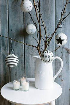 a white table topped with a vase filled with flowers and christmas ornaments next to a wooden wall