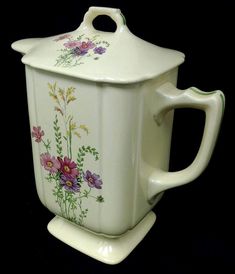 a white ceramic tea pot with flowers painted on the front and sides, sitting on a black background