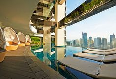 an outdoor swimming pool with lounge chairs and cityscape in the background