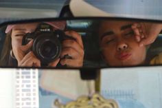 a woman taking a selfie in the side mirror of a car with her camera