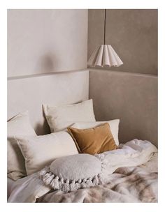 a bed with pillows and blankets on top of it next to a wall light hanging from the ceiling