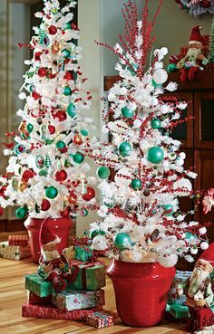 three white christmas trees with red, green and silver ornaments in pots on the floor