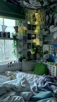 an unmade bed in front of a window with lots of pictures on the wall