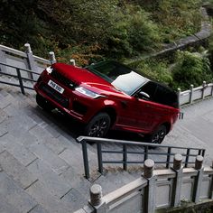 a red land rover parked on the side of a road next to a metal hand rail