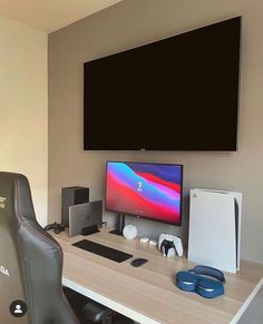 a computer desk with a monitor, keyboard and headphones on it in front of a flat screen tv