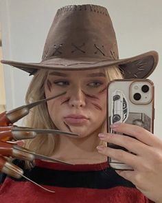 a woman wearing a cowboy hat and holding a cell phone with nails sticking out of her face