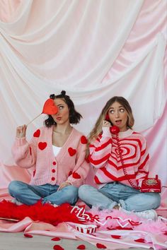 two women dressed in valentine's day outfits sit on the floor with candy and lollipop