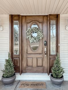 two potted plants sit in front of a wooden door with a wreath on it