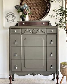 an old dresser is painted gray and has flowers on top, along with a wicker basket