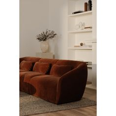 a brown couch sitting on top of a wooden floor next to a white book shelf