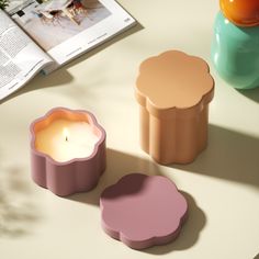 two candles sitting on top of a table next to an open book and vase with flowers