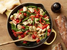 a skillet filled with vegetables and meat on top of a wooden table next to bread