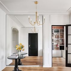 a room with a table, bookshelf and chandelier