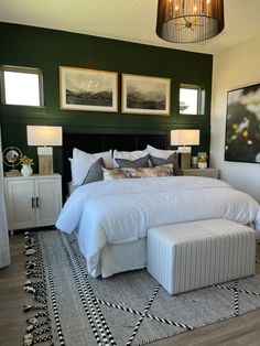 a bedroom with green walls and pictures on the wall above the bed, along with an ottoman