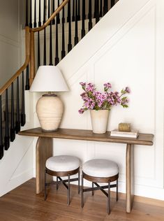 two stools and a table with flowers on it in front of a stair case