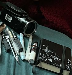 a camera, notebooks and pens are sitting on a bed