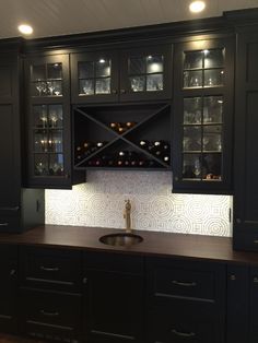 a kitchen with black cabinets and wine bottles in the cabinet doors, along with a sink