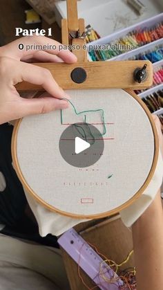 a person is holding a cross - stitch project in front of an easel with yarn and thread